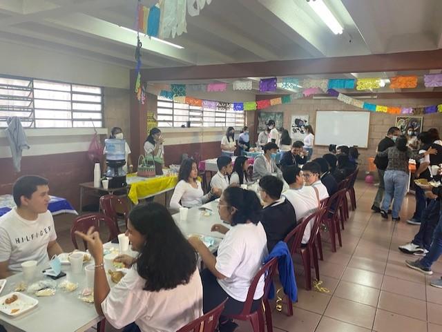 Estudiantes y familias comparten alimentos en mesas durante una actividad escolar.